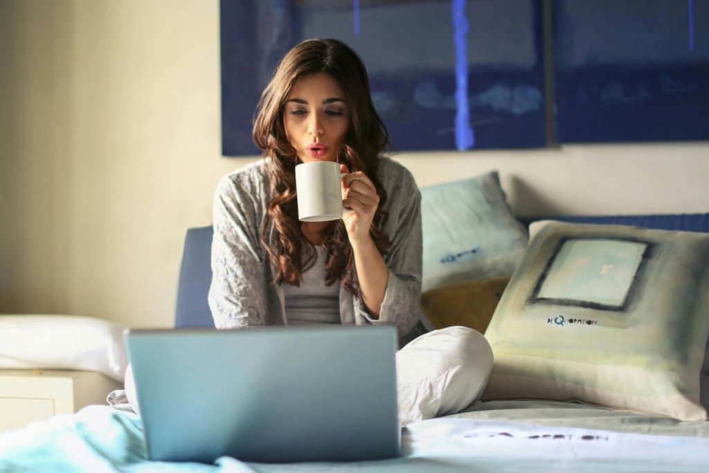 A woman drinking from a mug and using her laptop