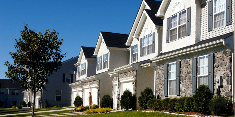 Row of modern townhouses with attached garages, stone and siding exterior, landscaped front yards, representing suburban residential housing.