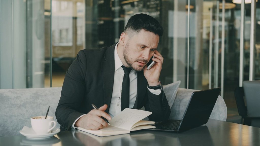 a person talks on the phone while writing notes in a cafe